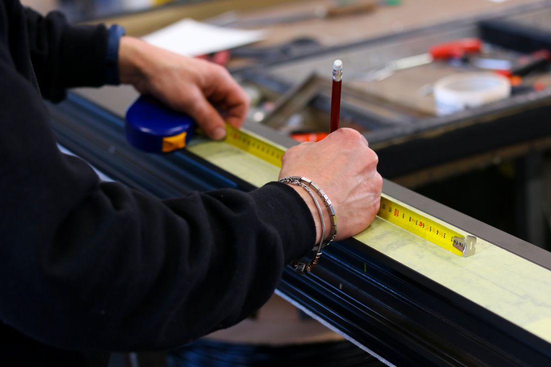 Rémy mesure un profilé aluminium au mètre ruban sur l'établi
